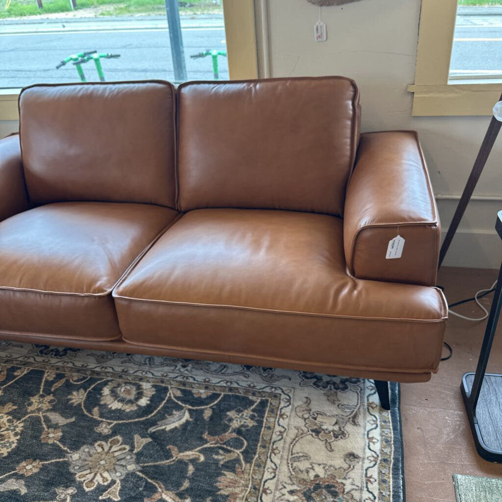 Brown leather sofa in a room with a patterned rug and window.