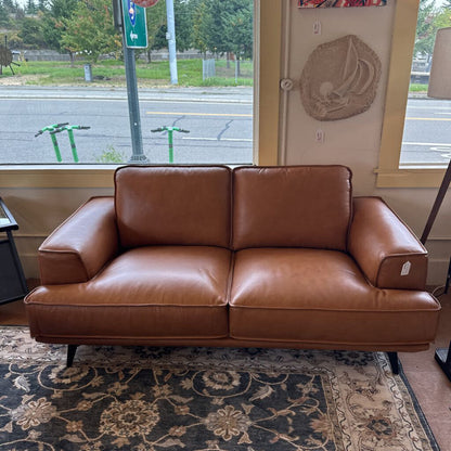 Brown leather sofa in a room with a window showing an outdoor view.