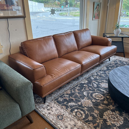 Brown leather sofa in a living room with a patterned rug and a window in the background.