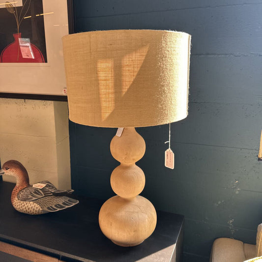 Wooden lamp with a beige lampshade on a dark surface against a blue wall.