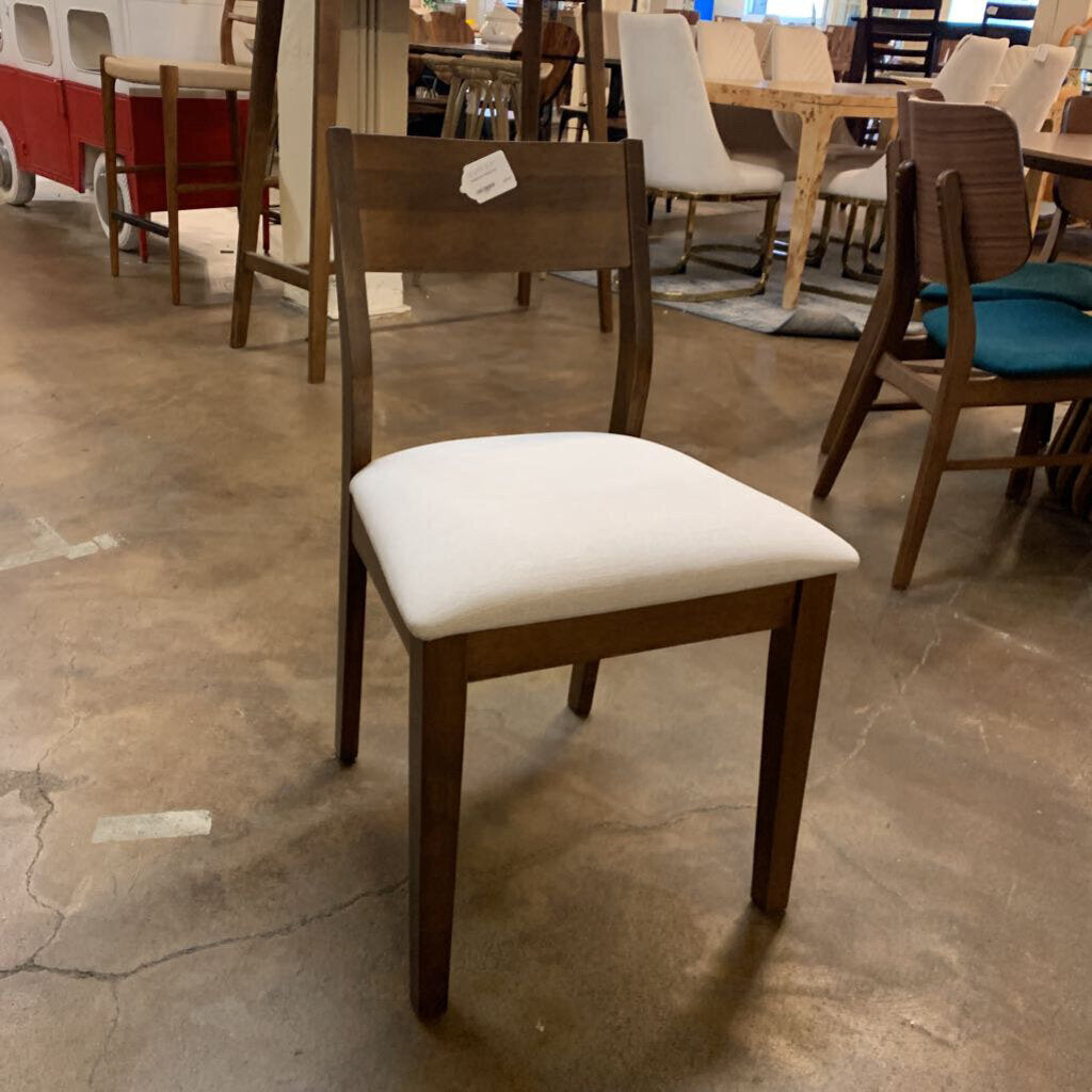 Wooden chair with a white cushion on a concrete floor in a showroom setting.