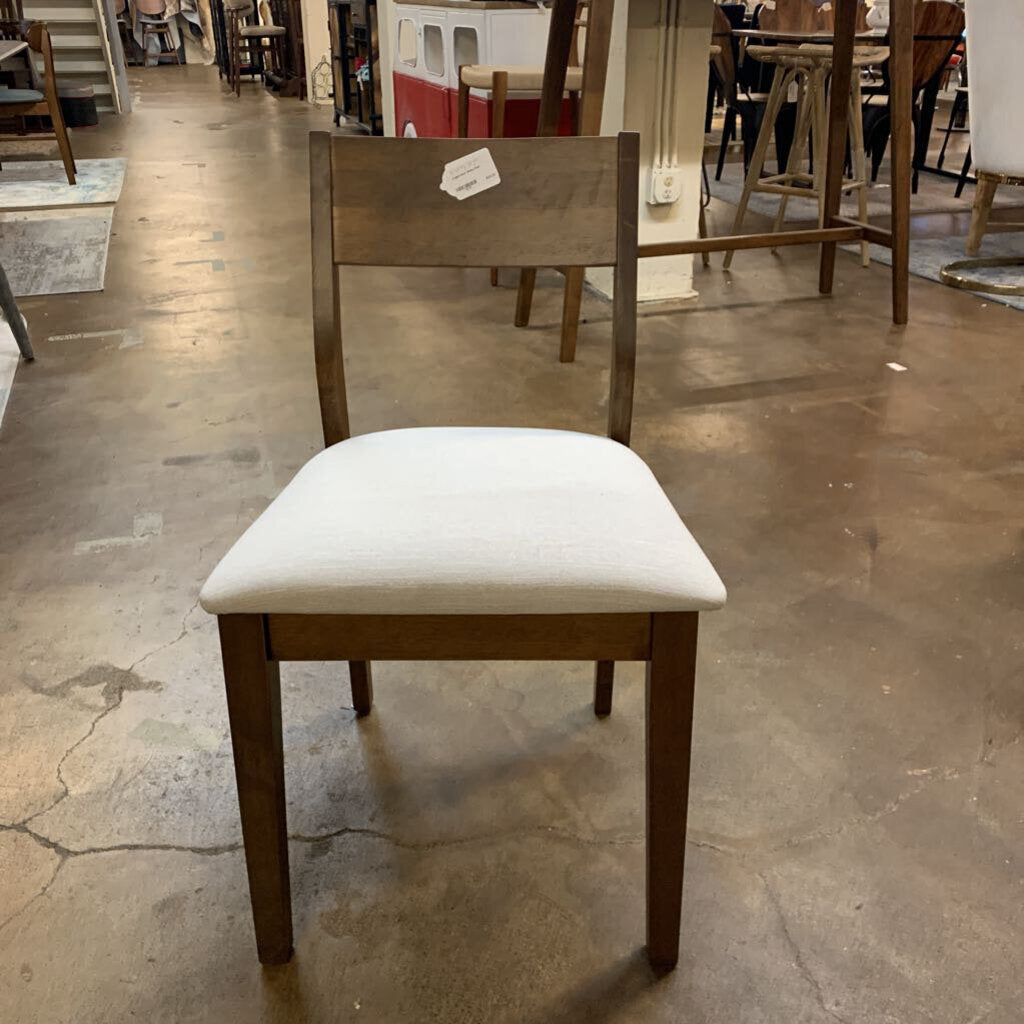 Wooden chair with a white cushion on a concrete floor in a warehouse setting.