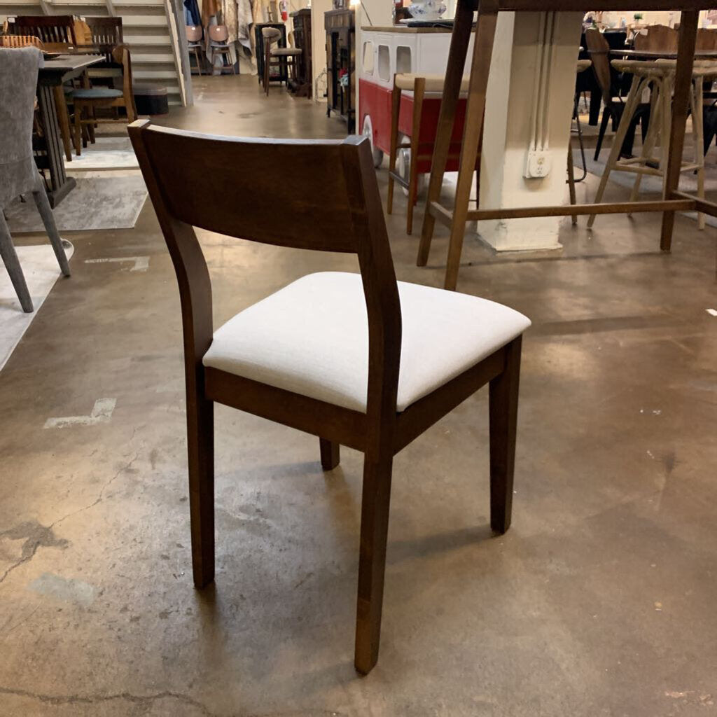 Wooden chair with a white cushion on a concrete floor in an indoor setting