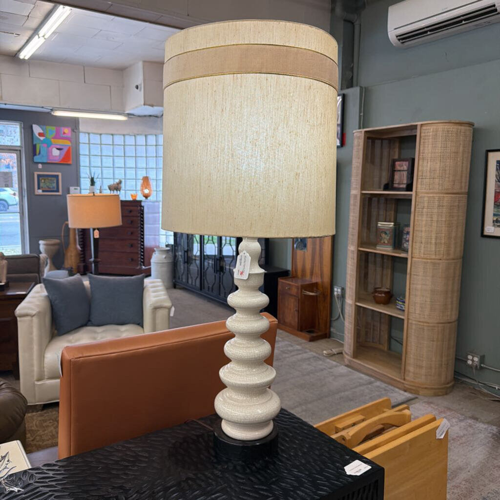 Table lamp with a beige shade on a table in a room with furniture and decor.