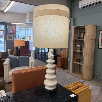 Table lamp with a beige shade on a table in a room with furniture and decor.