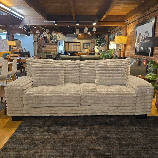 Beige sofa in a room with wooden walls and ceiling, chairs, and tables.