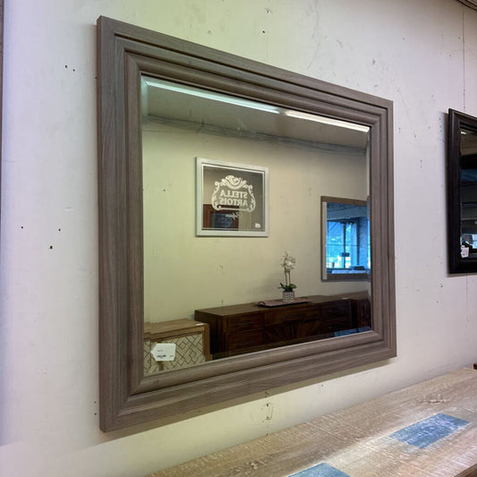 Large wooden-framed mirror on a white wall with reflections of decor items.