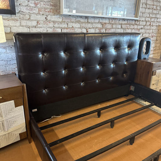 Black tufted headboard on a wooden floor with a brick wall background