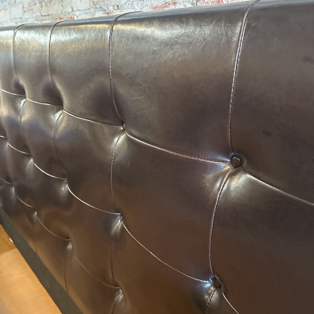 Close-up of a brown leather headboard with tufted design.