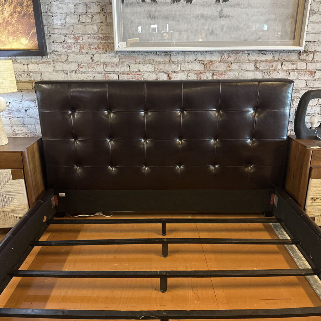 Brown leather bed frame on a wooden floor with a brick wall background