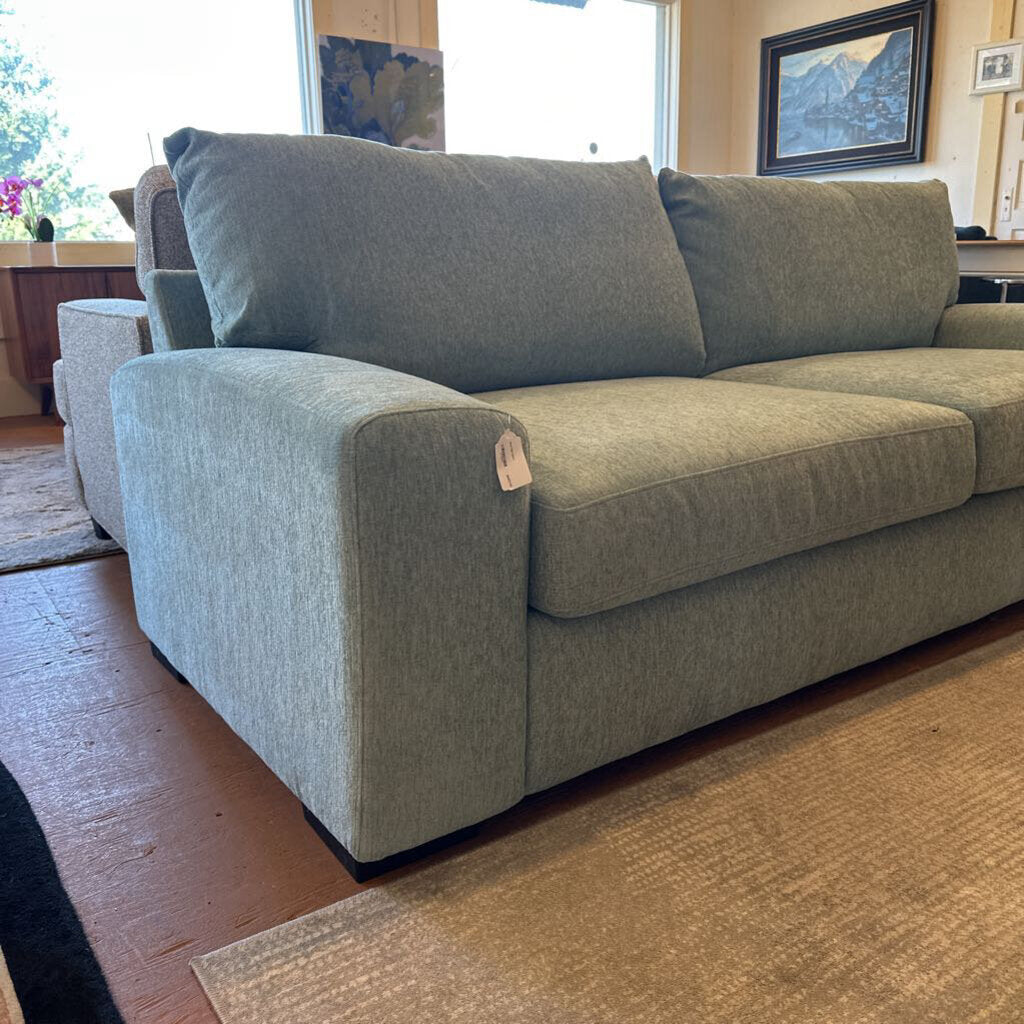 Gray sofa in a living room setting with a wooden floor and windows.
