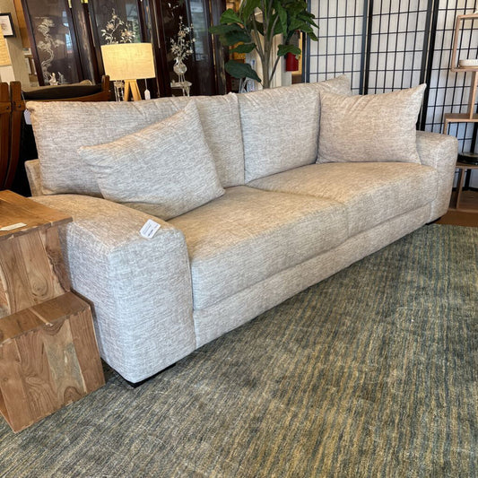 Beige sofa with cushions on a carpeted floor in a room setting.