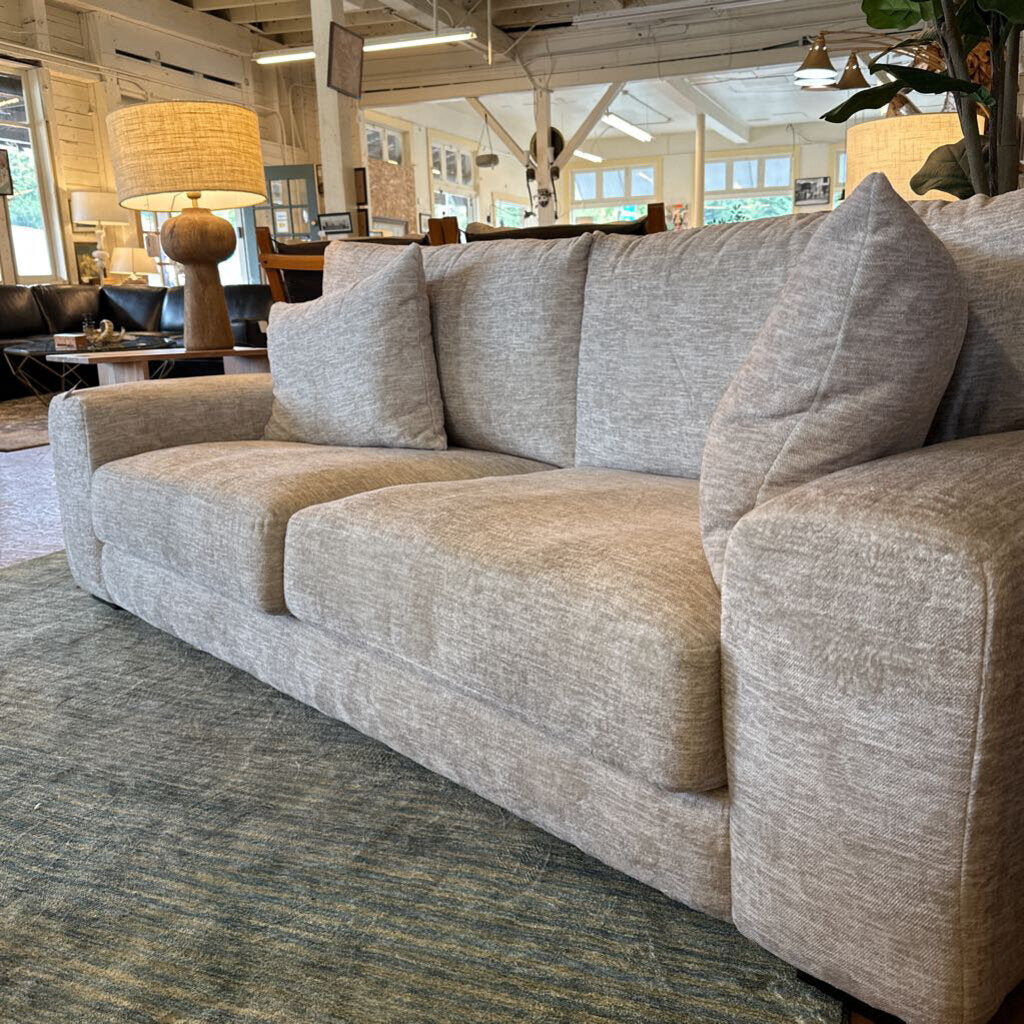 Gray sofa in a room with a lamp and chairs in the background