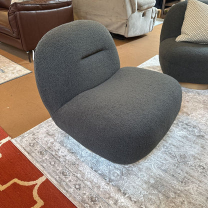 Gray textured chair on a patterned rug with a brown couch and beige armchair in the background.
