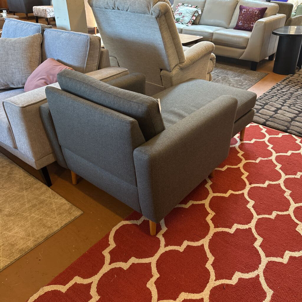 Gray armchair on a red patterned rug with a living room setting in the background