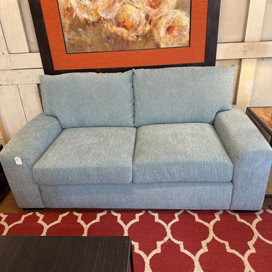 Gray sofa in a room with a red and white patterned rug and a painting on the wall.
