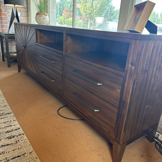 Wooden dresser with starburst design in a room with a rug and window view.