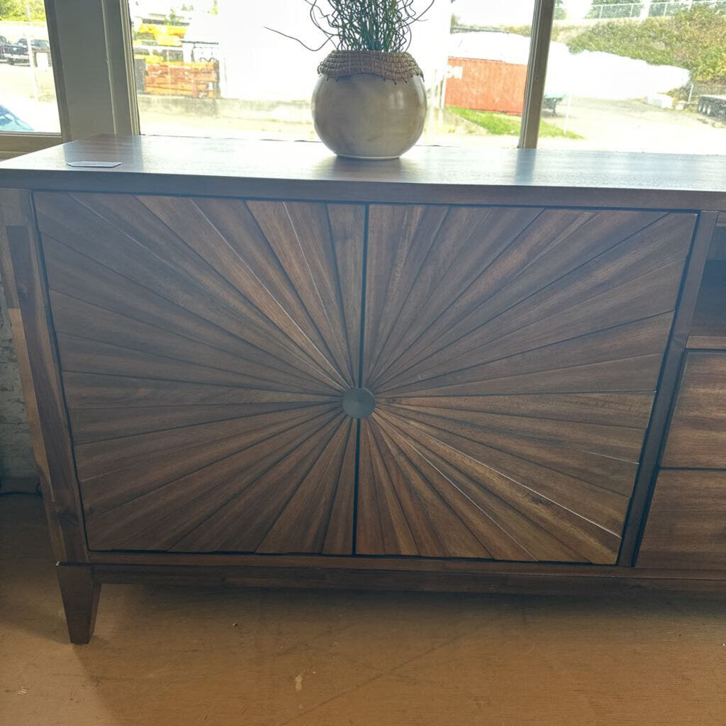 Wooden cabinet with sunburst design in a room with a window and plant.