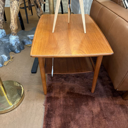 Wooden side table with a brown rug and furniture in the background
