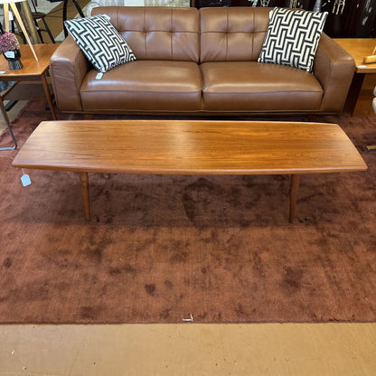 Brown leather sofa with patterned cushions and a wooden coffee table on a brown rug.