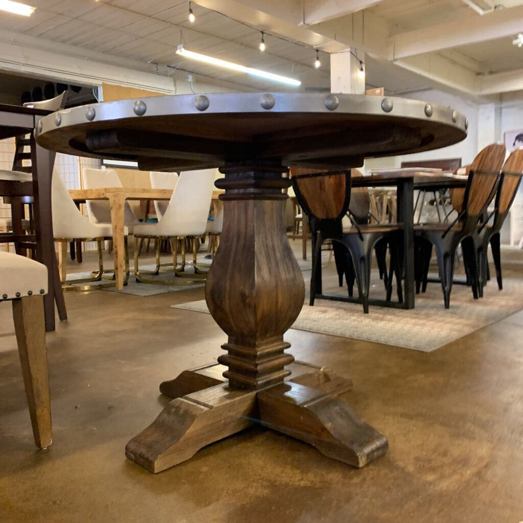 Wooden dining table with a round top and pedestal base in a showroom setting.