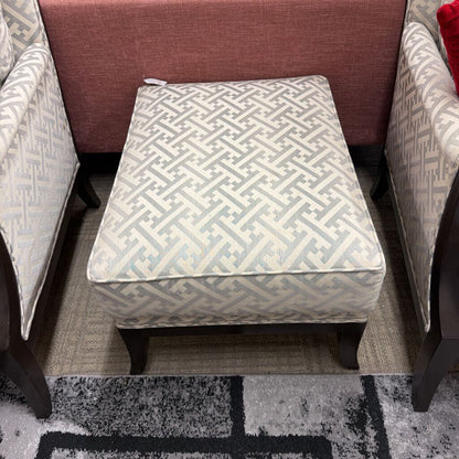 Patterned ottoman in a living room setting with chairs and a rug.