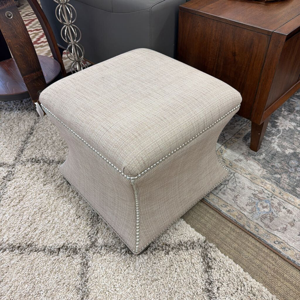 Beige ottoman on a patterned rug with wooden furniture in the background