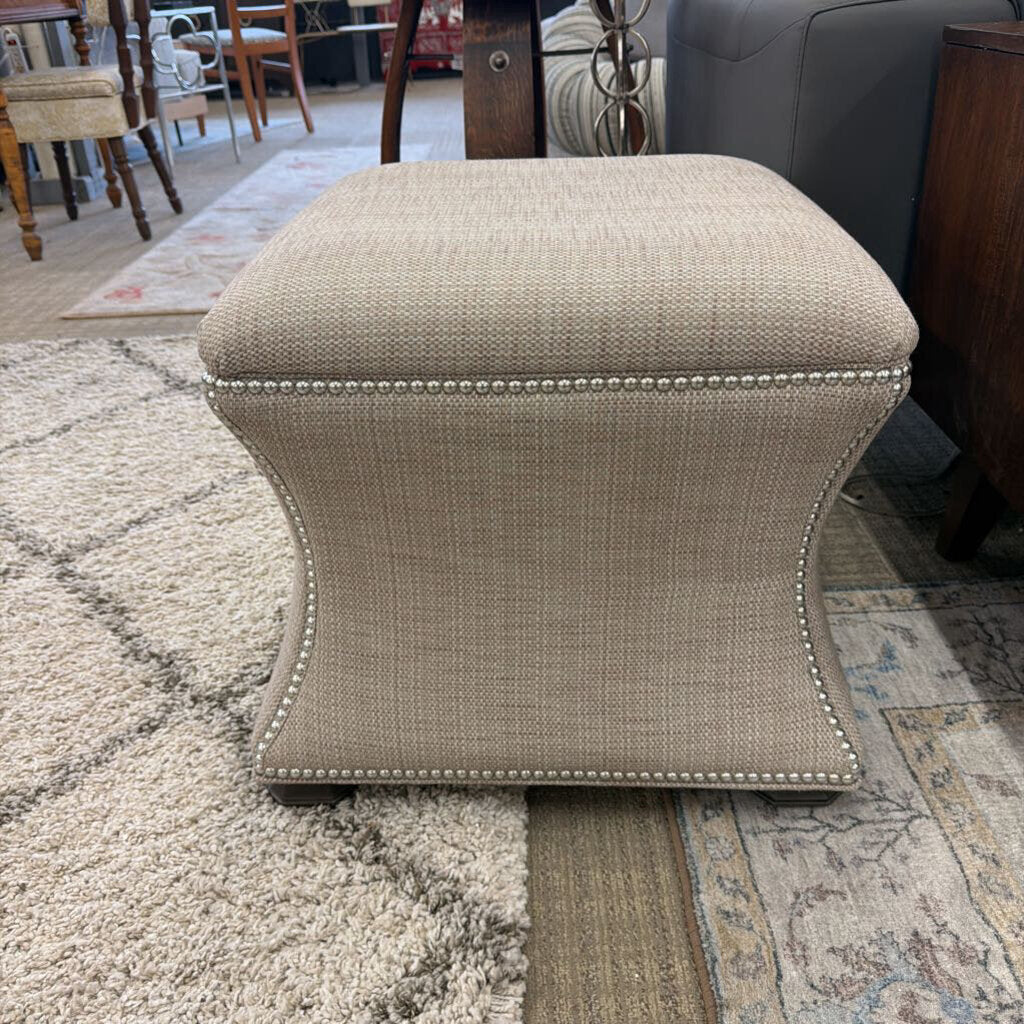 Beige ottoman with nailhead trim on a patterned rug