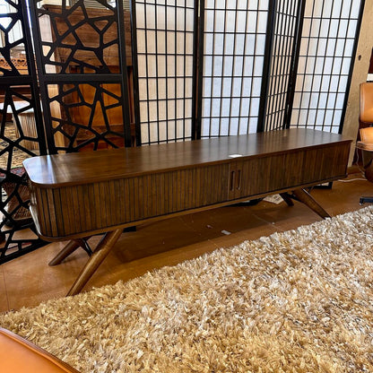 Wooden console table in a room with a textured rug and decorative screen.