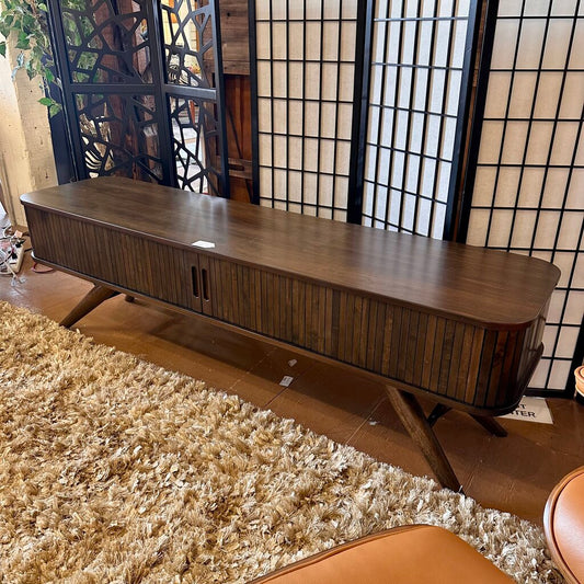 Wooden TV stand in a room with a textured rug and decorative screen.
