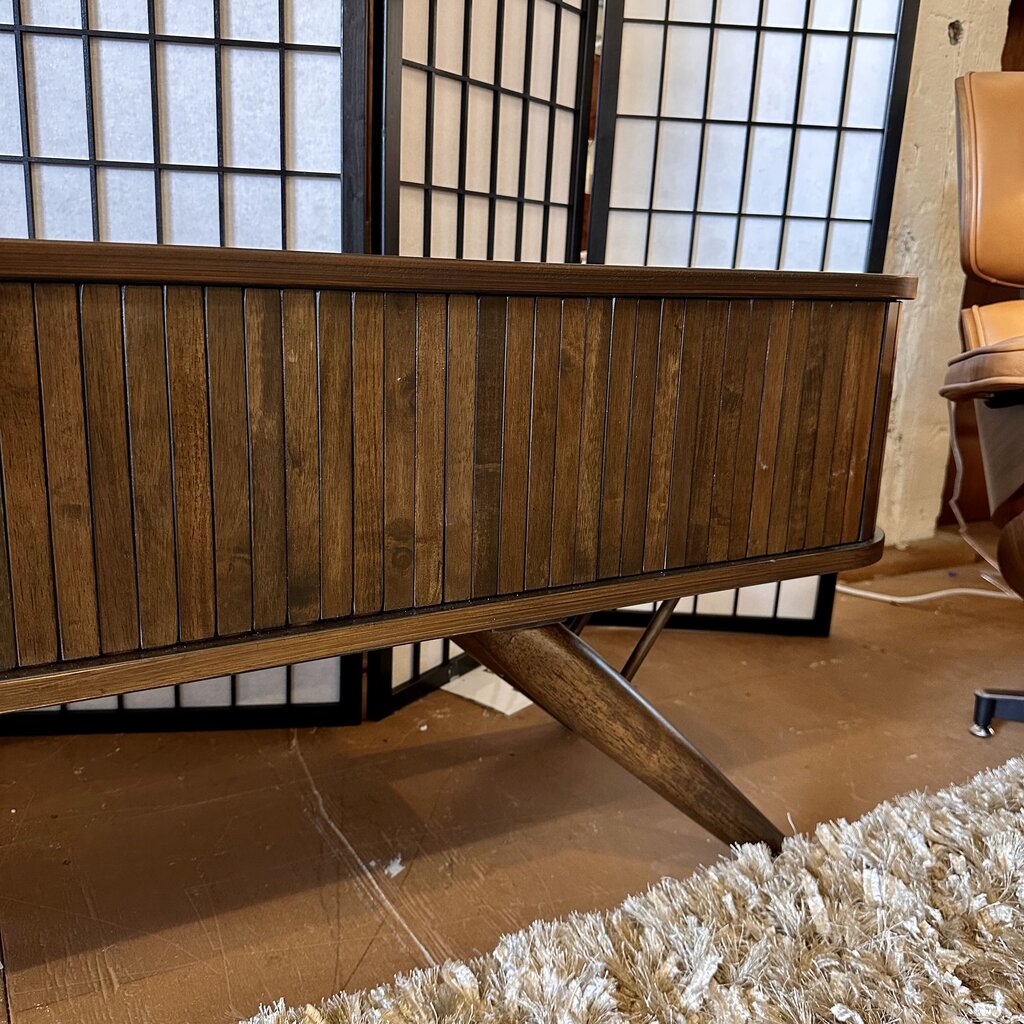 Wooden sideboard with a chair and rug in a room with large windows.