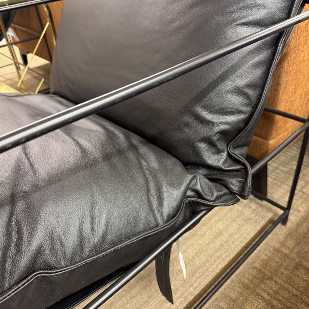 Close-up of a black leather chair with metal frame on a wooden floor.