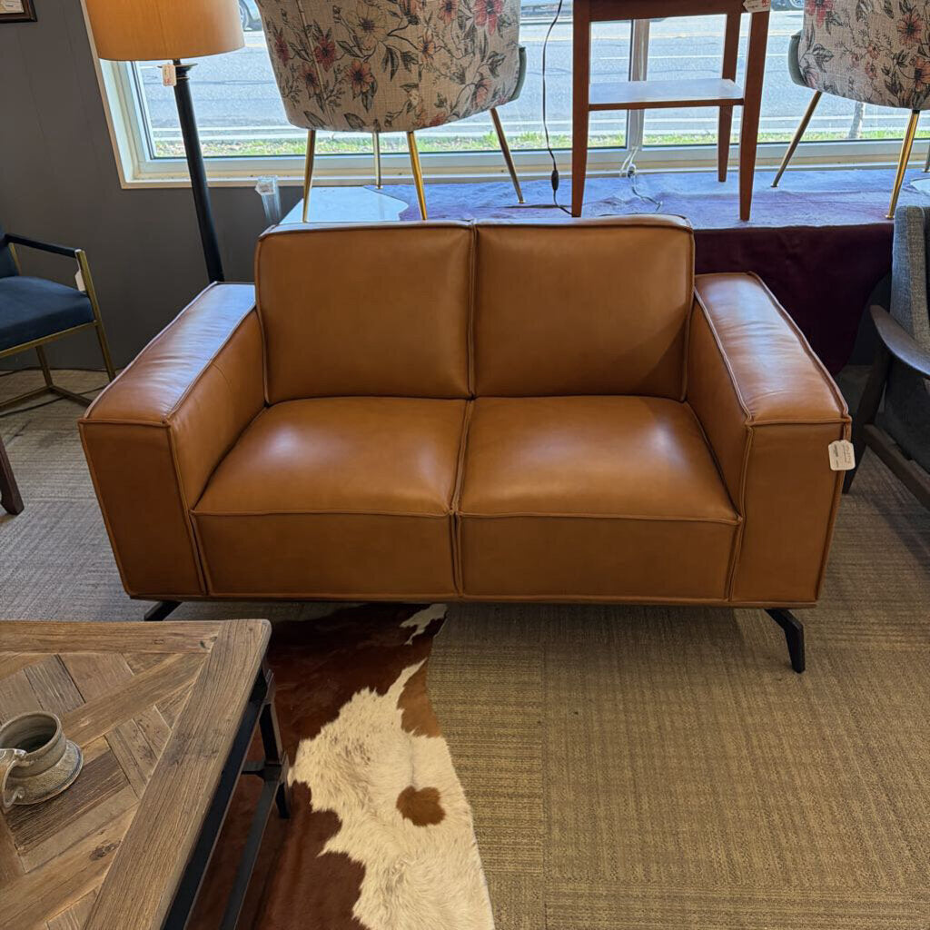 Brown leather sofa in a room with a coffee table and chairs.