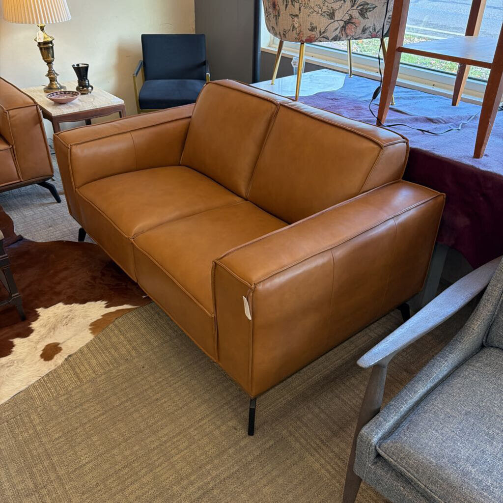 Brown leather sofa in a living room setting with chairs and a lamp.