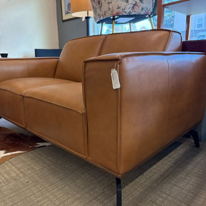 Brown leather sofa with a tag in a room with a rug and lamp.