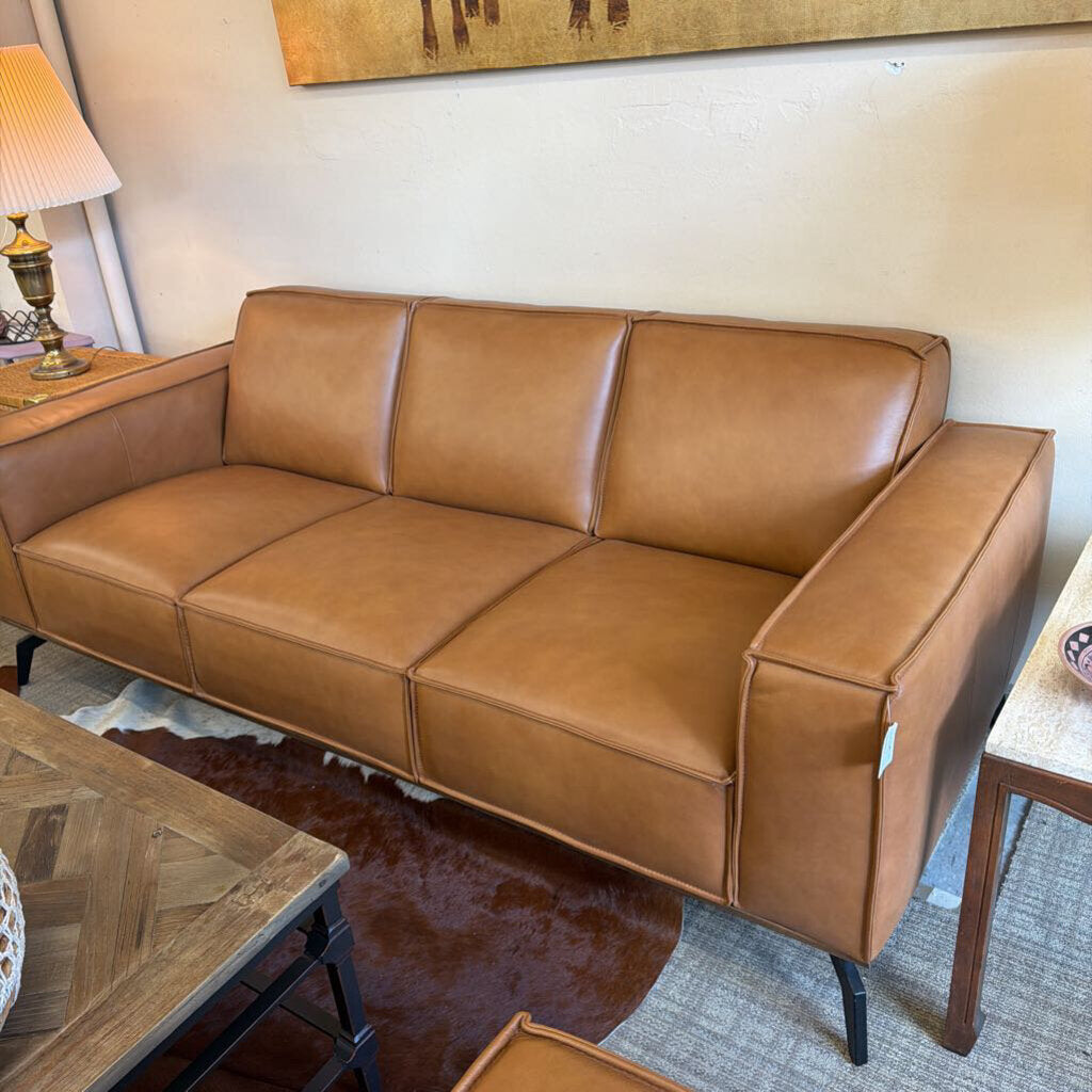 Brown leather sofa in a living room setting with a lamp and coffee table.