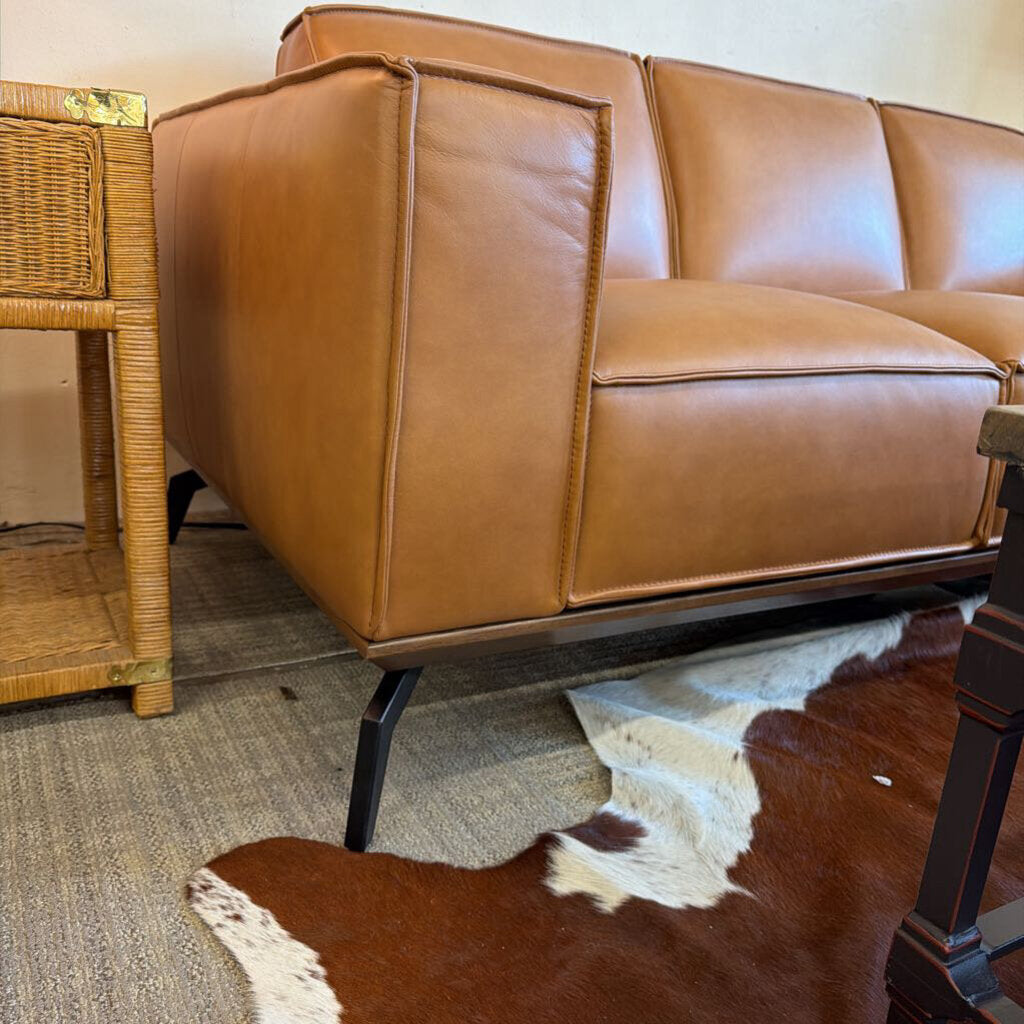 Brown leather sofa in a room with a cowhide rug and wicker side table.