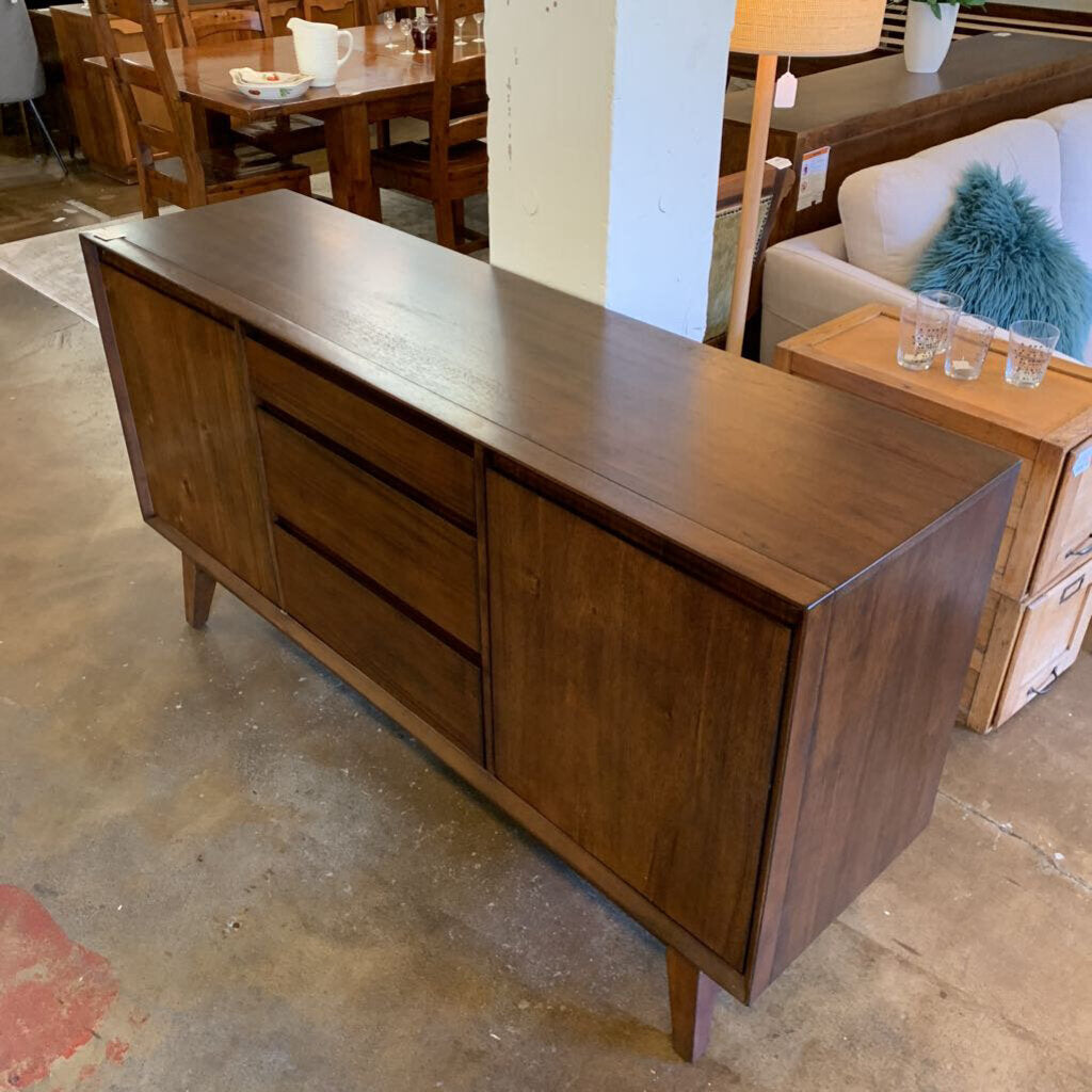 Wooden sideboard in a showroom setting with furniture and decor items around.