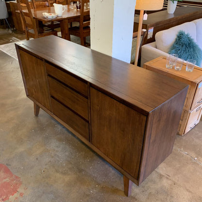 Wooden sideboard in a showroom setting with furniture and decor items around.