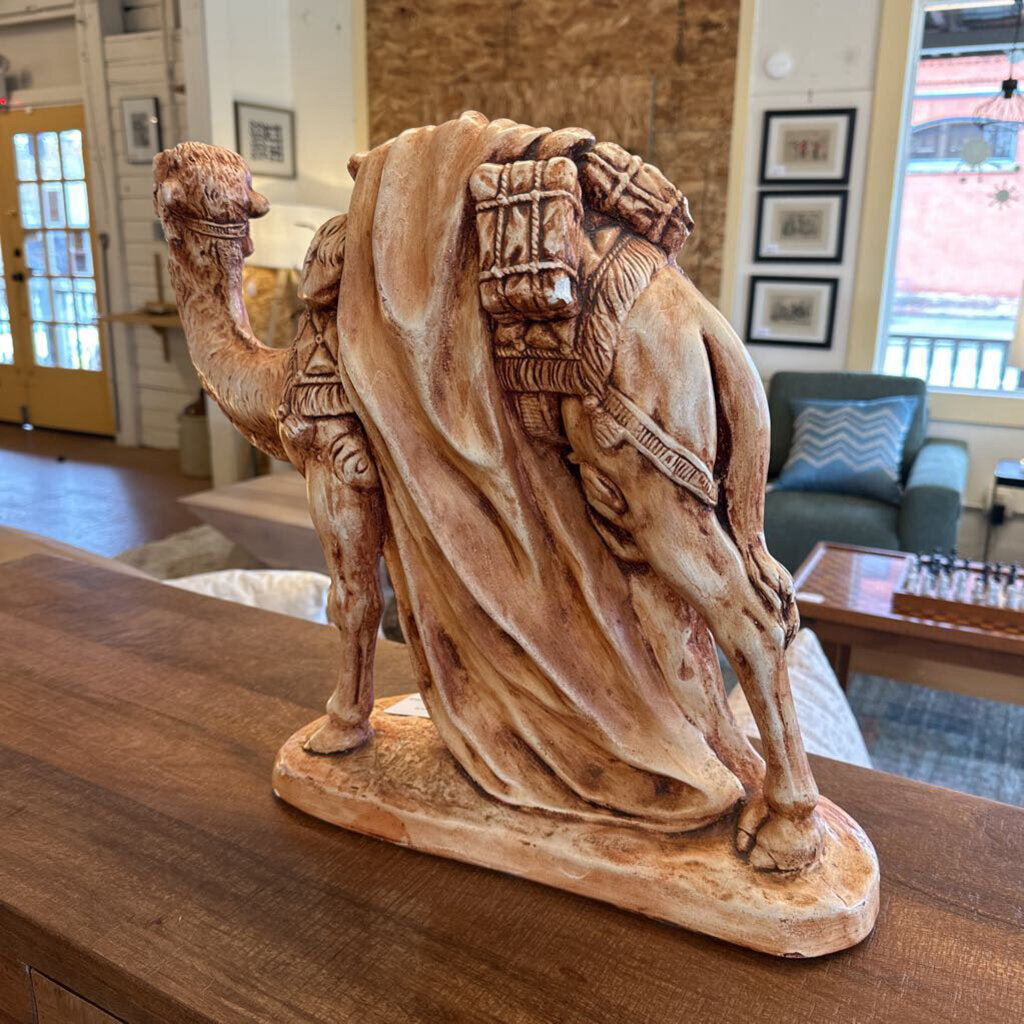 Camel statue with a saddle on a wooden surface in a room with furniture and decor.