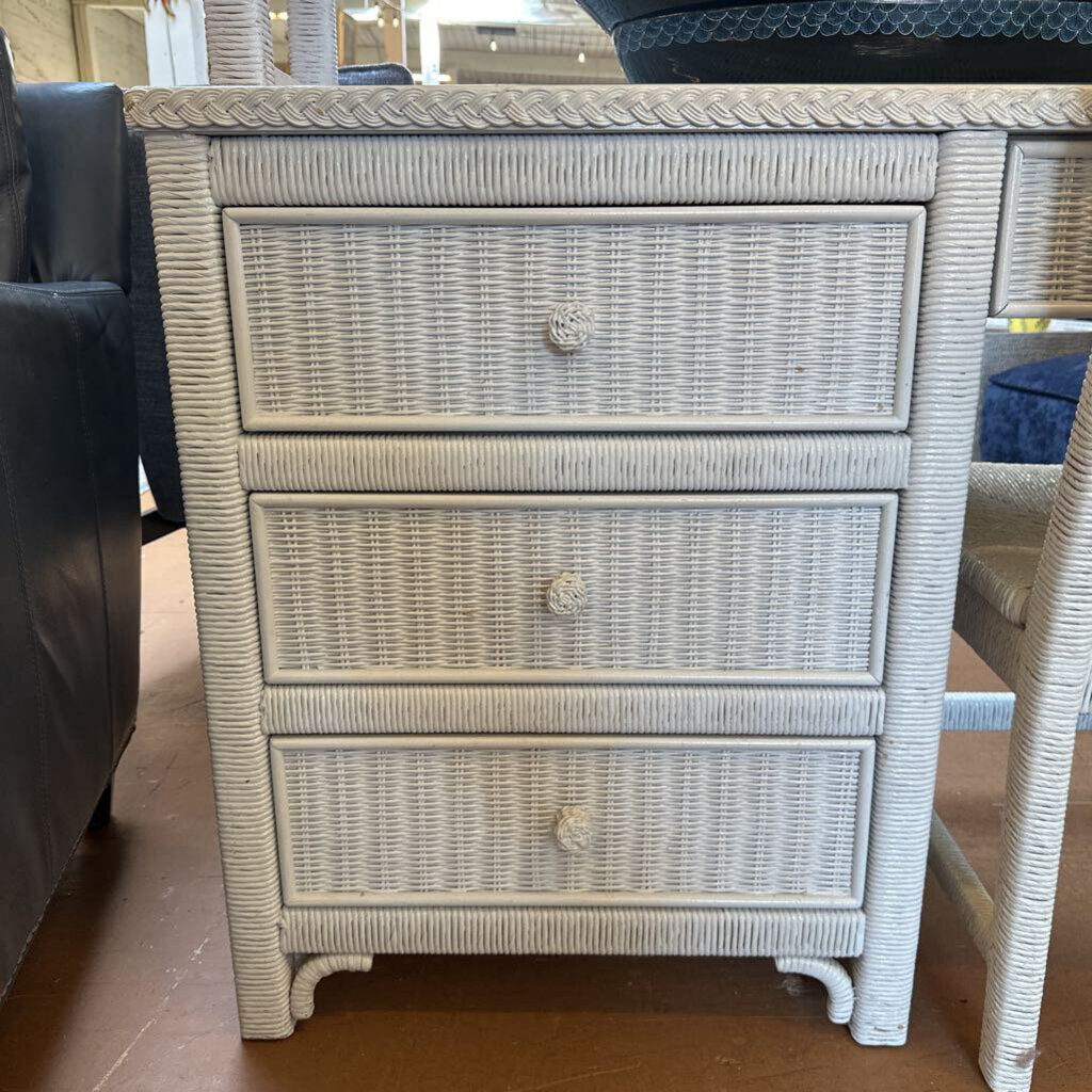 Wicker nightstand with three drawers on a wooden floor.