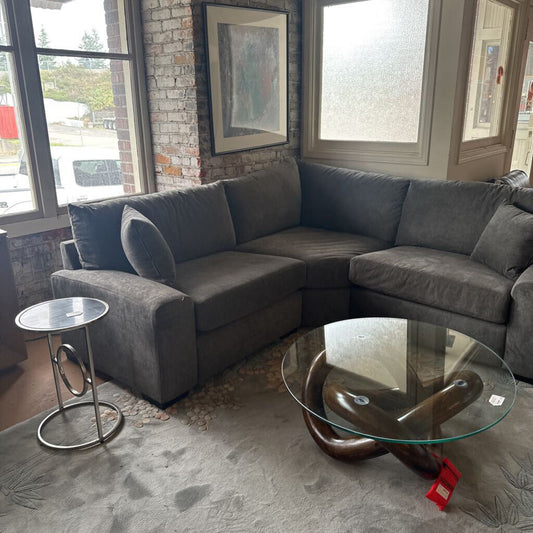 Gray sectional sofa in a living room with a glass coffee table and side table.