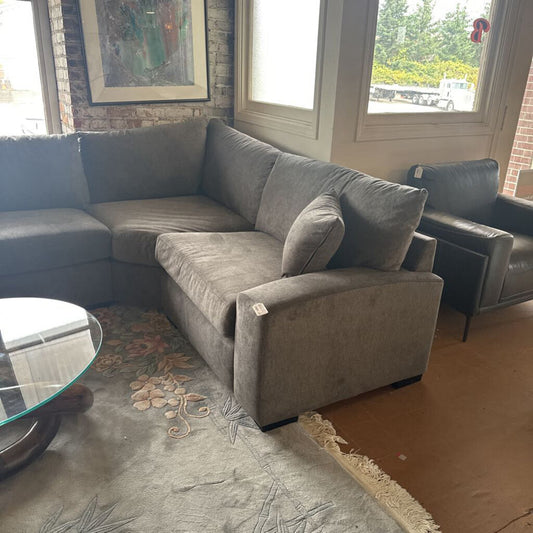 Gray sectional sofa in a living room with a rug and window.