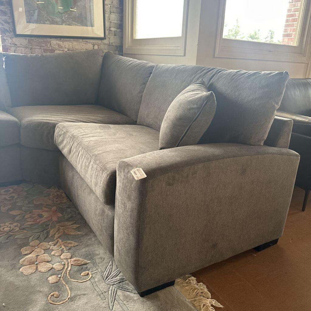 Gray sectional sofa in a living room with a patterned rug and windows.