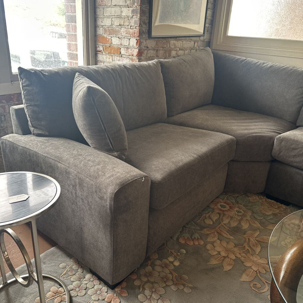 Gray sectional sofa in a living room with a brick wall and window in the background.