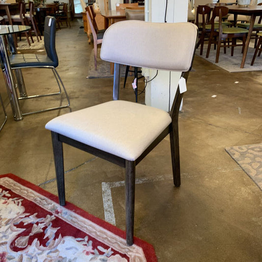 Chair with beige cushioned seat and backrest in a store setting with tables and chairs.