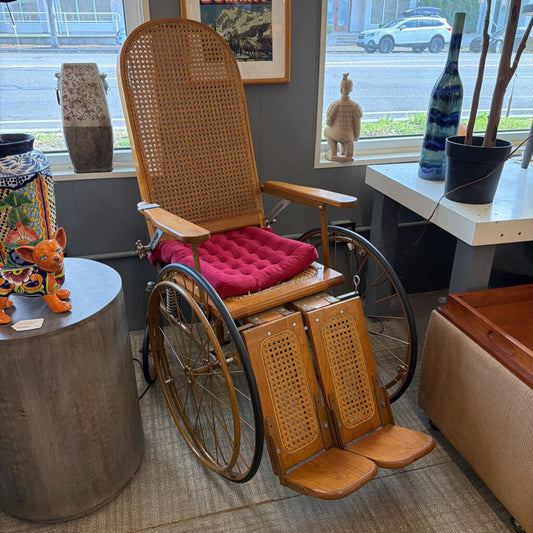 Wooden wheelchair with wicker backrest and red cushion in a room with decor elements.