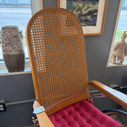 Wicker chair with pink cushion in a room with framed pictures on the wall.