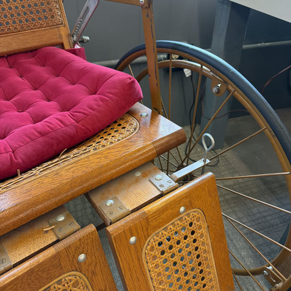 Close-up of an antique wooden vehicle seat with a pink cushion and large wheel.