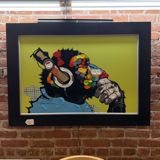 Framed artwork of a stylized character with a colorful head and guitar on a brick wall.